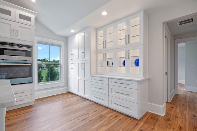 interior space with white cabinetry, double oven, and vaulted ceiling