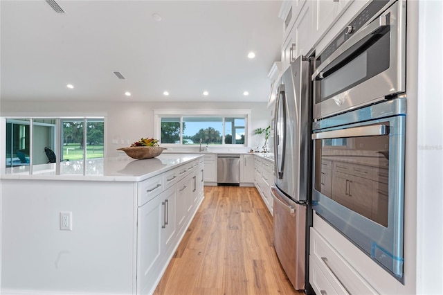 kitchen featuring light stone countertops, white cabinets, stainless steel appliances, and light hardwood / wood-style floors