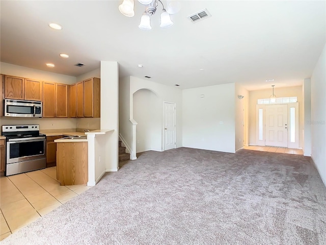 kitchen with an inviting chandelier, light colored carpet, hanging light fixtures, and appliances with stainless steel finishes