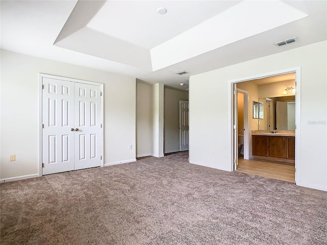 unfurnished bedroom with connected bathroom, carpet flooring, a raised ceiling, and a closet