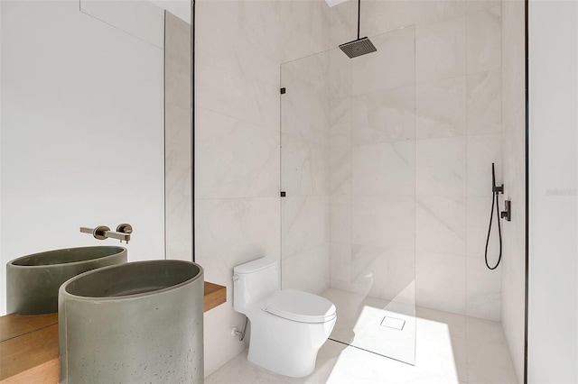 bathroom with toilet, a tile shower, and tile walls