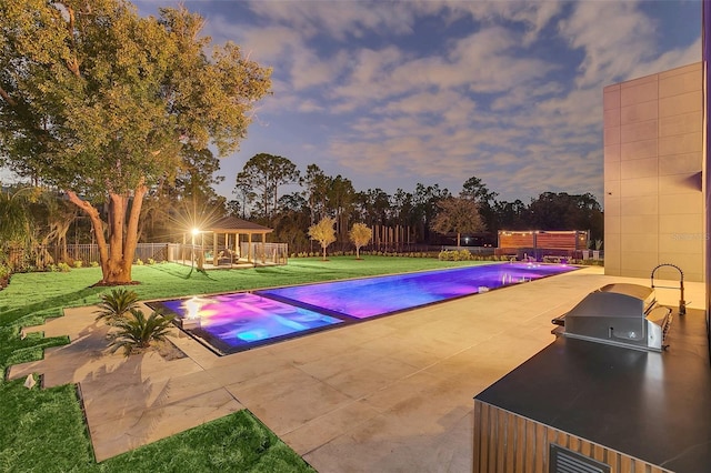 pool at dusk with exterior kitchen, a patio area, and a yard