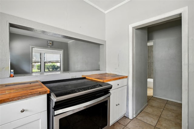 kitchen featuring wood counters, white cabinets, stainless steel range with electric cooktop, ornamental molding, and light tile patterned floors