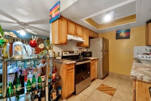 kitchen featuring ceiling fan, appliances with stainless steel finishes, backsplash, a tray ceiling, and light tile patterned flooring