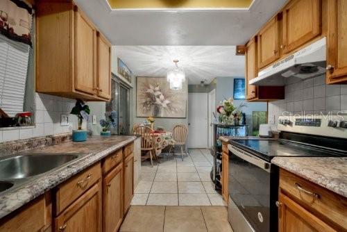 kitchen with tasteful backsplash, stainless steel electric range oven, decorative light fixtures, and light tile patterned floors