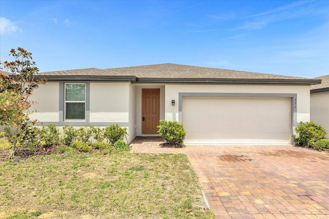 ranch-style house featuring stucco siding, an attached garage, a shingled roof, and decorative driveway