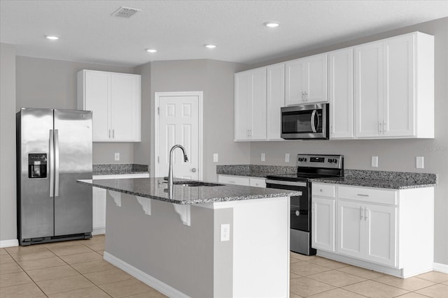 kitchen featuring dark stone countertops, visible vents, a kitchen island with sink, a sink, and stainless steel appliances