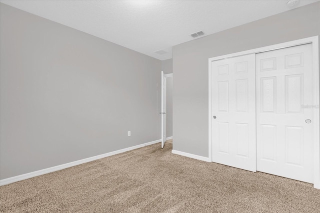 unfurnished bedroom featuring visible vents, a textured ceiling, a closet, baseboards, and light colored carpet