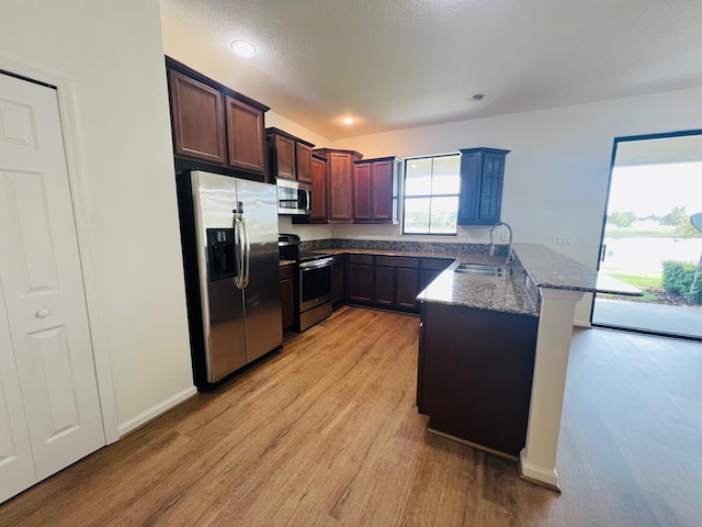 kitchen featuring sink, dark stone countertops, light wood-type flooring, appliances with stainless steel finishes, and kitchen peninsula