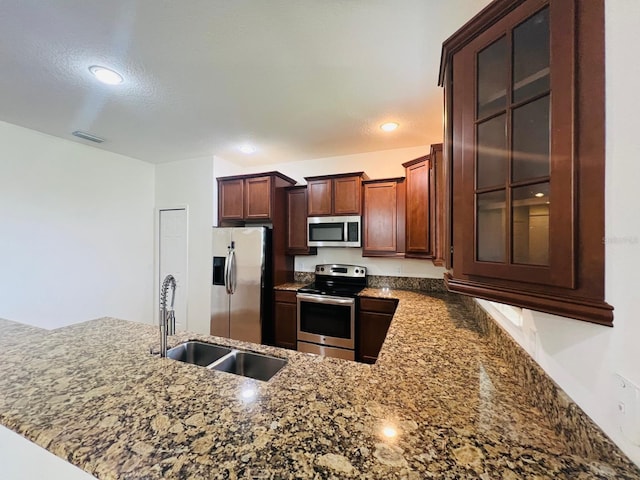 kitchen featuring sink, dark stone countertops, a textured ceiling, appliances with stainless steel finishes, and kitchen peninsula