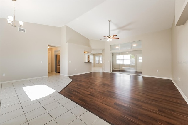 unfurnished living room featuring ceiling fan with notable chandelier, light tile patterned floors, and vaulted ceiling