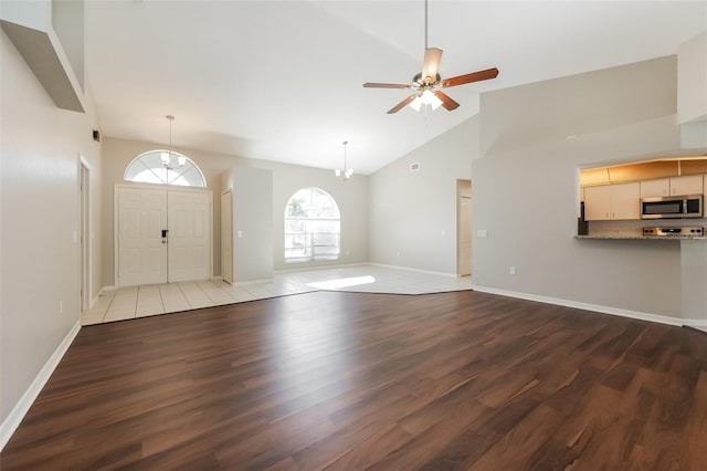 unfurnished living room with ceiling fan with notable chandelier, wood-type flooring, and high vaulted ceiling