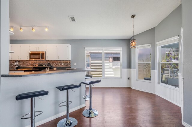 kitchen with appliances with stainless steel finishes, white cabinets, backsplash, and dark wood-type flooring