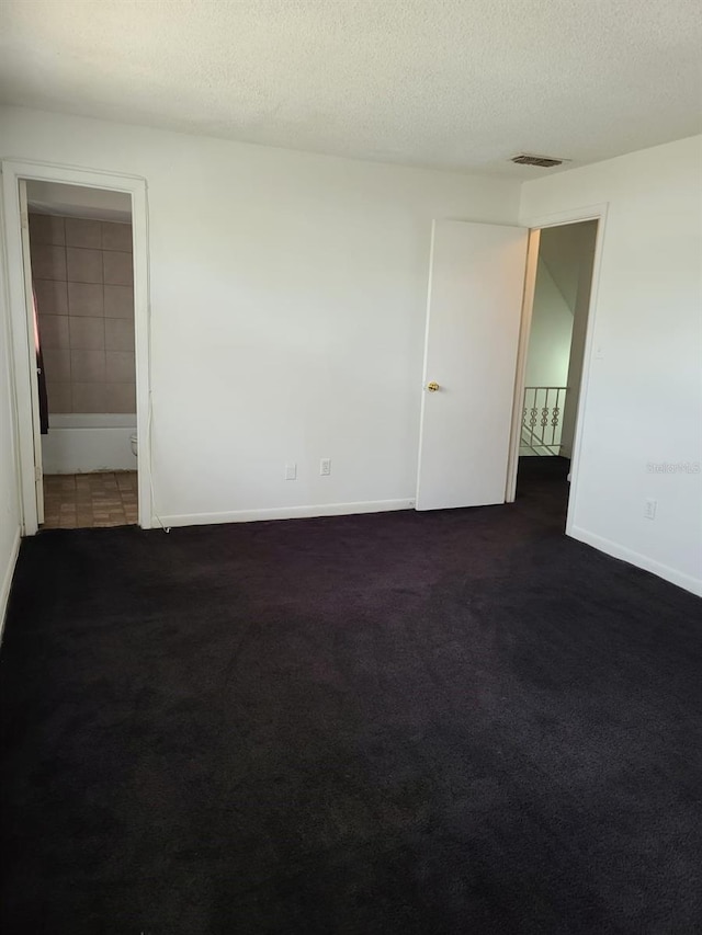 spare room featuring dark colored carpet and a textured ceiling