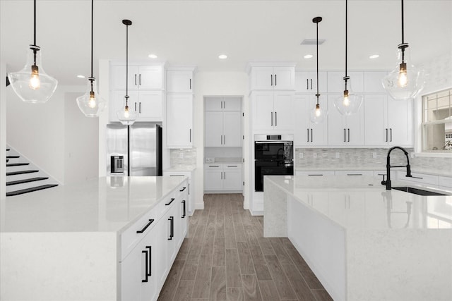 kitchen with sink, stainless steel fridge, black double oven, decorative light fixtures, and white cabinets