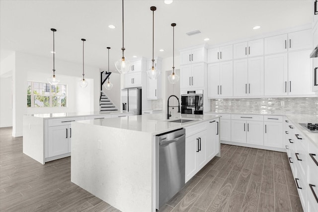 kitchen with a center island with sink, hanging light fixtures, and appliances with stainless steel finishes