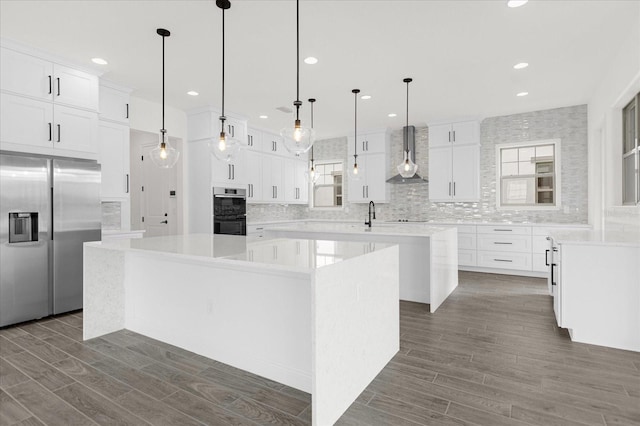 kitchen featuring wall chimney exhaust hood, a large island, white cabinets, and stainless steel appliances