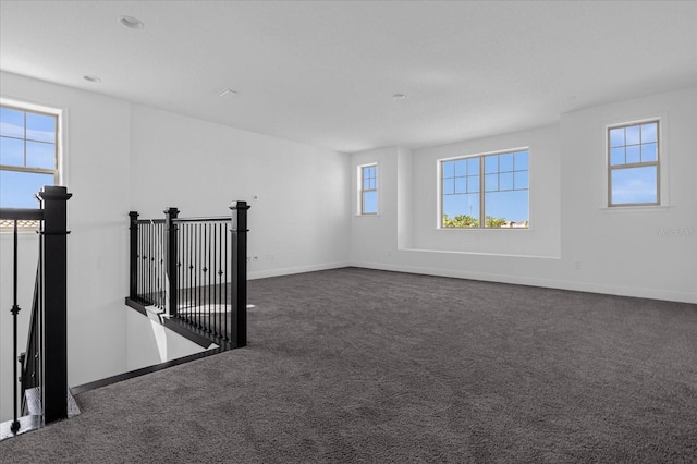 empty room featuring dark carpet and a wealth of natural light