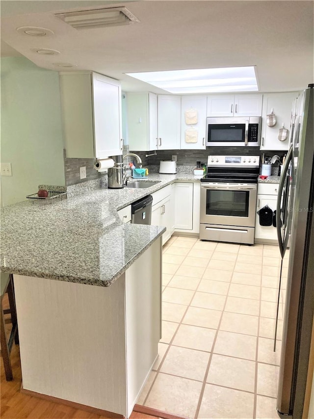 kitchen featuring sink, kitchen peninsula, light stone countertops, white cabinetry, and stainless steel appliances