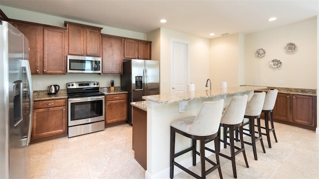 kitchen featuring light tile patterned flooring, stainless steel appliances, a breakfast bar area, light stone counters, and kitchen peninsula