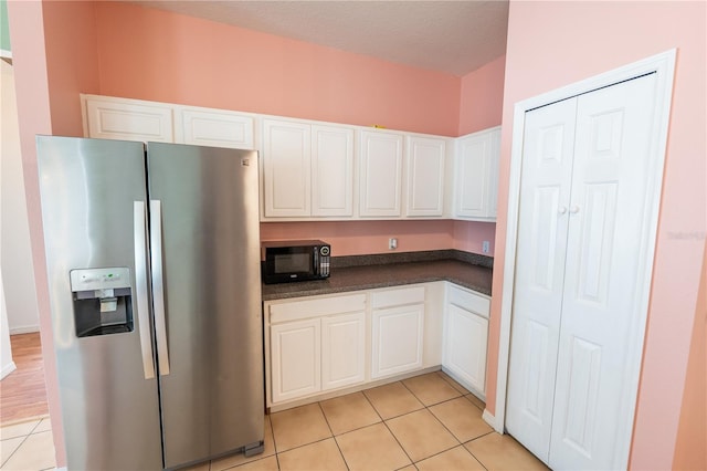 kitchen with stainless steel fridge, light tile patterned floors, a textured ceiling, and white cabinetry