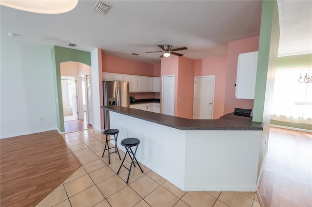 kitchen with stainless steel fridge, kitchen peninsula, white cabinetry, and light tile patterned floors