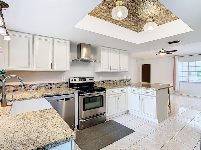 kitchen featuring white cabinets, wall chimney range hood, hanging light fixtures, sink, and appliances with stainless steel finishes