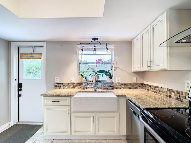 kitchen with wall chimney range hood, sink, light stone countertops, light tile patterned floors, and stainless steel appliances