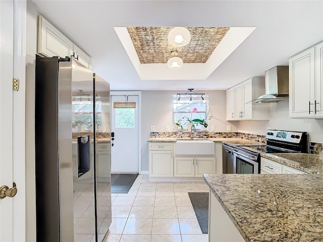 kitchen with wall chimney exhaust hood, stainless steel appliances, a raised ceiling, sink, and light tile patterned flooring