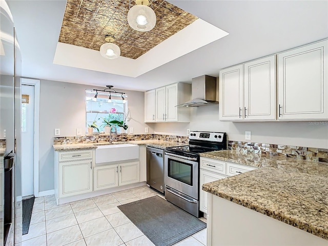 kitchen with wall chimney exhaust hood, stainless steel appliances, sink, white cabinetry, and light tile patterned flooring