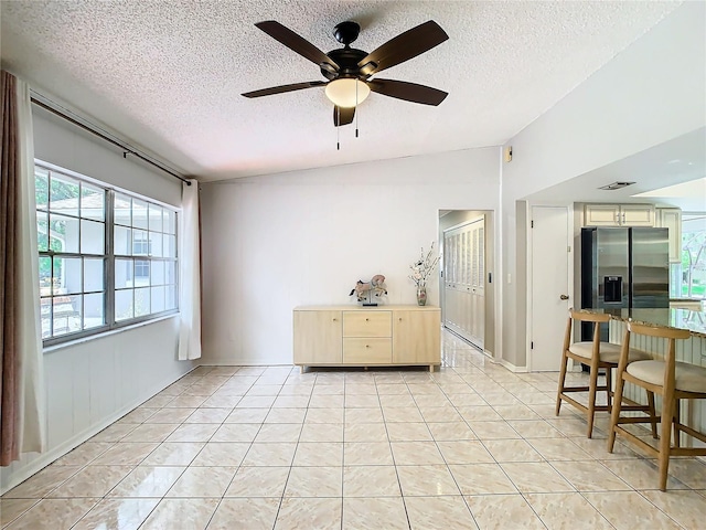 interior space featuring ceiling fan, light tile patterned floors, a textured ceiling, and vaulted ceiling