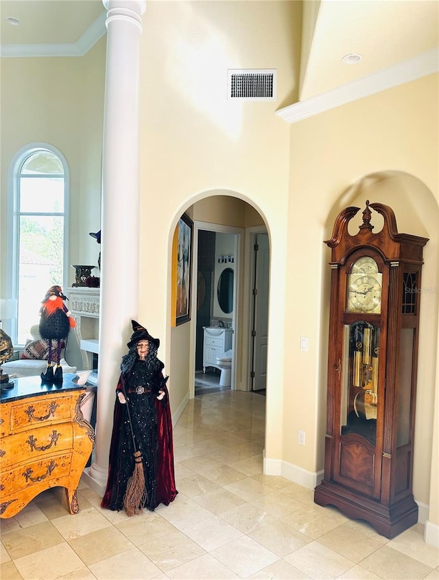 hallway featuring baseboards, visible vents, a high ceiling, arched walkways, and ornamental molding