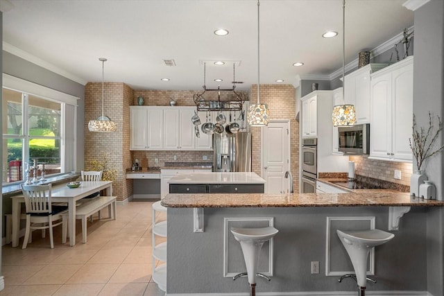 kitchen with brick wall, appliances with stainless steel finishes, decorative light fixtures, white cabinetry, and ornamental molding