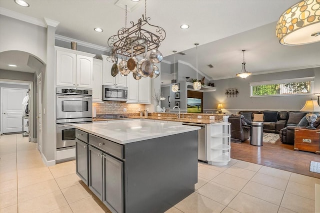 kitchen with pendant lighting, appliances with stainless steel finishes, ornamental molding, white cabinets, and kitchen peninsula