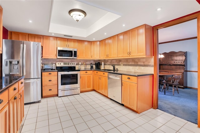 kitchen featuring sink, a raised ceiling, tasteful backsplash, light tile patterned flooring, and appliances with stainless steel finishes