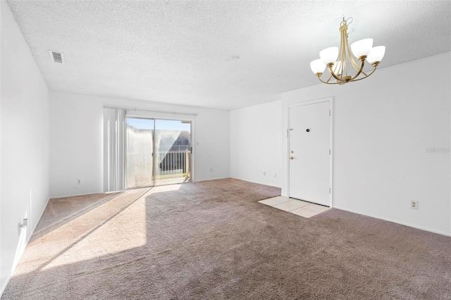 carpeted empty room featuring a textured ceiling and a chandelier