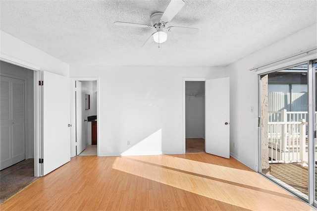 unfurnished bedroom featuring ceiling fan, access to outside, a textured ceiling, a spacious closet, and light hardwood / wood-style flooring