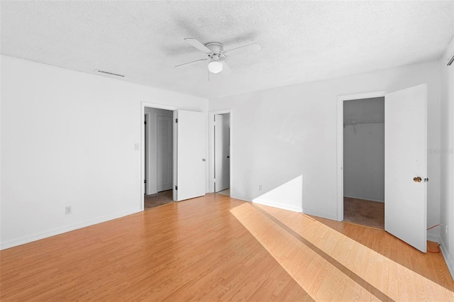 unfurnished bedroom featuring ceiling fan, a textured ceiling, a spacious closet, light hardwood / wood-style floors, and a closet