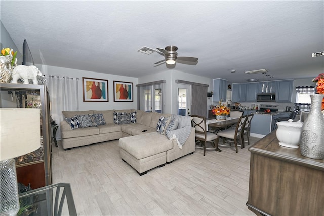 living room featuring light hardwood / wood-style floors, sink, a textured ceiling, and ceiling fan