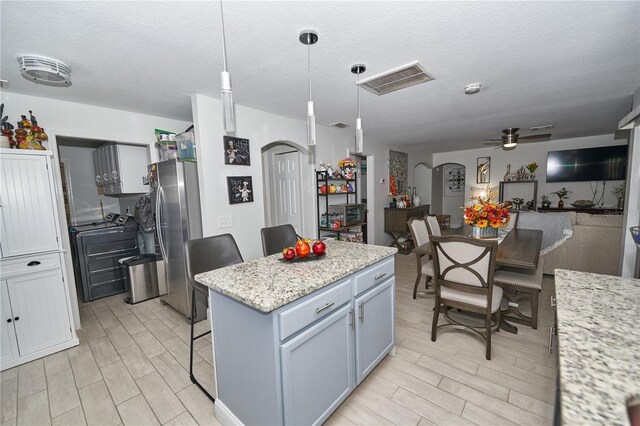 kitchen with decorative light fixtures, ceiling fan, a center island, light stone counters, and stainless steel refrigerator