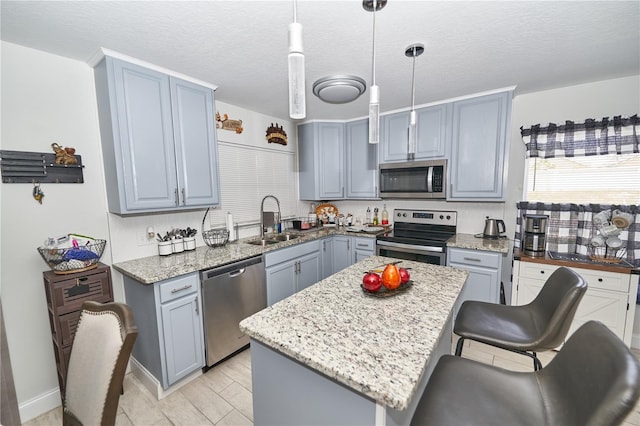 kitchen featuring a textured ceiling, a center island, appliances with stainless steel finishes, pendant lighting, and sink