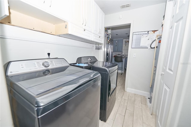 laundry area featuring washer and dryer, light hardwood / wood-style flooring, and cabinets