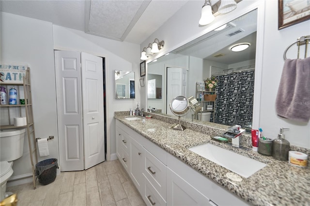 bathroom with wood-type flooring, double sink vanity, toilet, and a textured ceiling