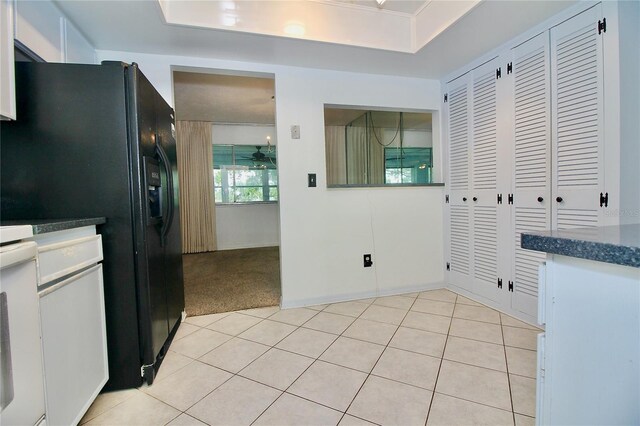 kitchen featuring a tray ceiling, black refrigerator with ice dispenser, oven, and light tile patterned flooring