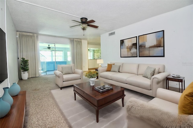 living room with ceiling fan, light carpet, and a textured ceiling