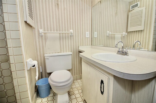 bathroom with vanity, toilet, and wallpapered walls