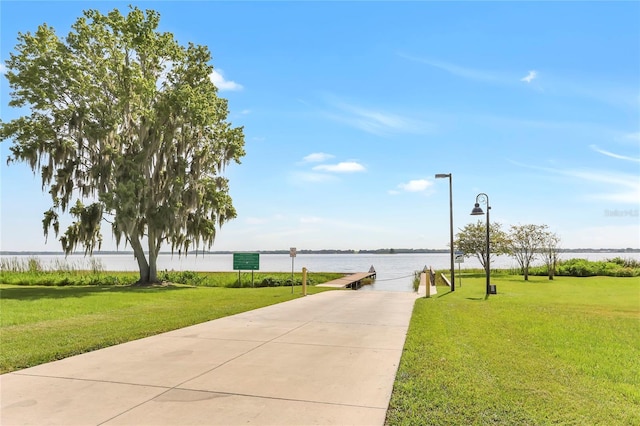 view of home's community with a water view, a lawn, and a boat dock