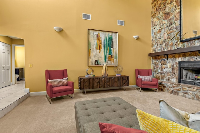 sitting room featuring light colored carpet, a stone fireplace, and a towering ceiling