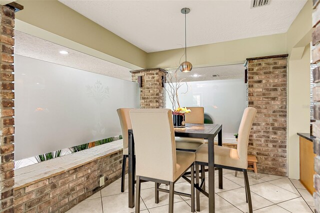 tiled dining area with decorative columns, brick wall, and a textured ceiling