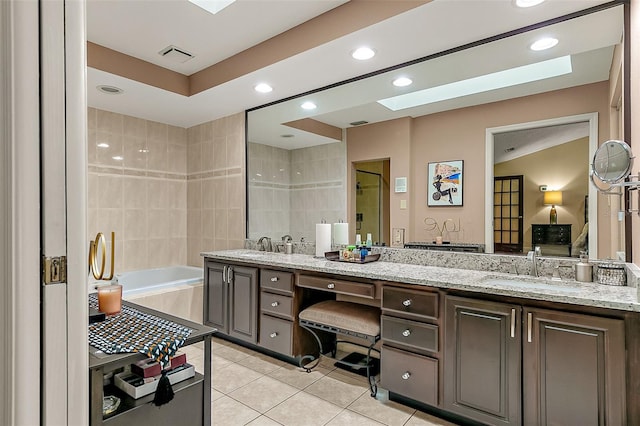 bathroom with tile patterned floors, tiled bath, a skylight, and vanity